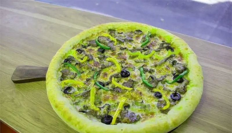 پیتزای پرملات و جذاب پیتزایی بلا با ترکیبی بی‌نظیر از گوشت، پنیر آب شده، فلفل دلمه‌ای رنگارنگ و زیتون سیاه، روی تخته چوبی.