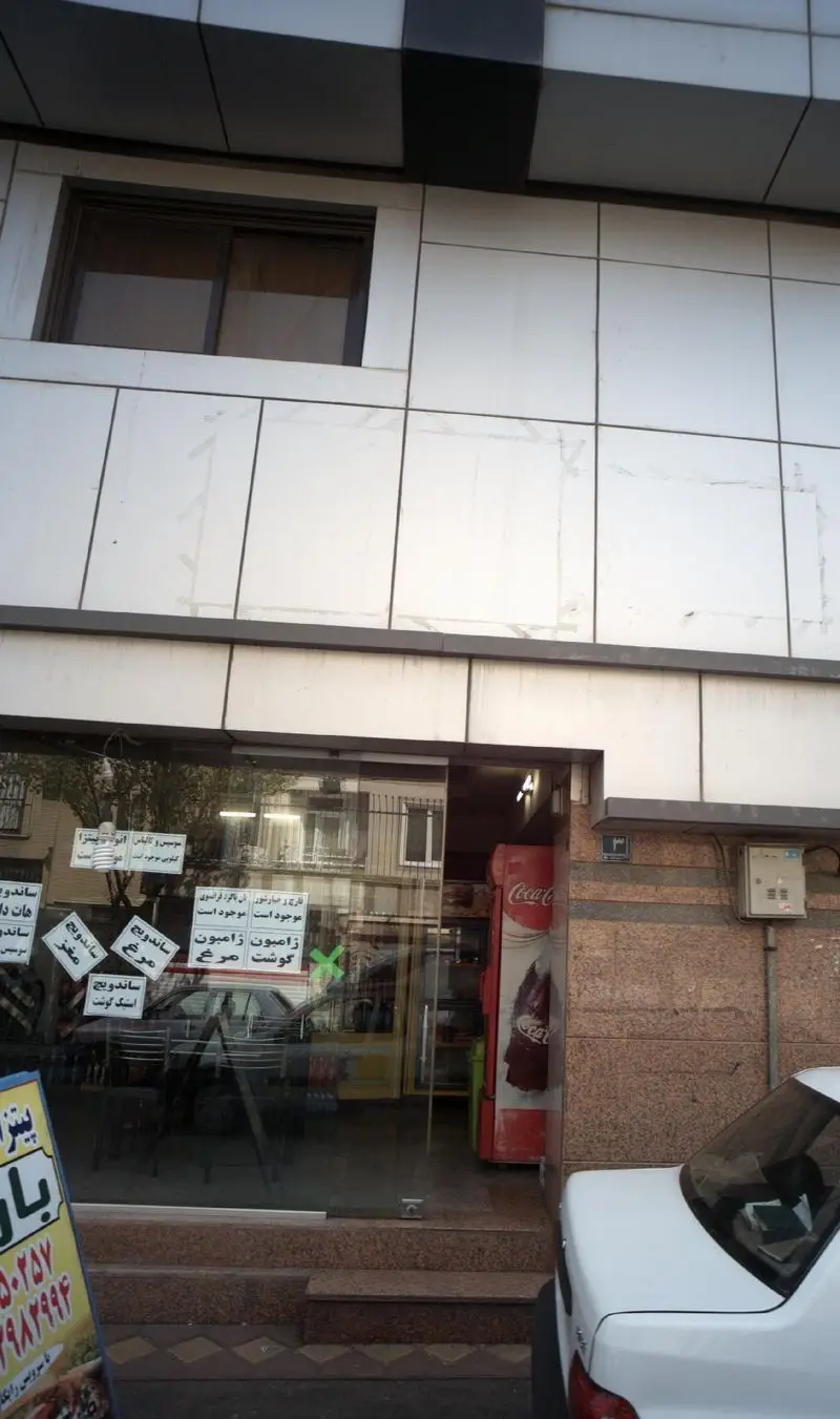 نمای بیرونی و ورودی شیشه ای فست فود پیتزا ساندویچ باران با تابلو منوی متنوع شامل انواع پیتزا و ساندویچ‌های مرغ، ژامبون و استیک.