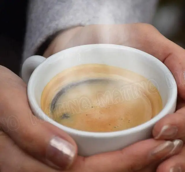 دستان گرمی که فنجانی از قهوه اسپرسو داغ و معطر را با بخار ملایم در کافه جلاتو متینو با عشق نگه داشته‌اند.