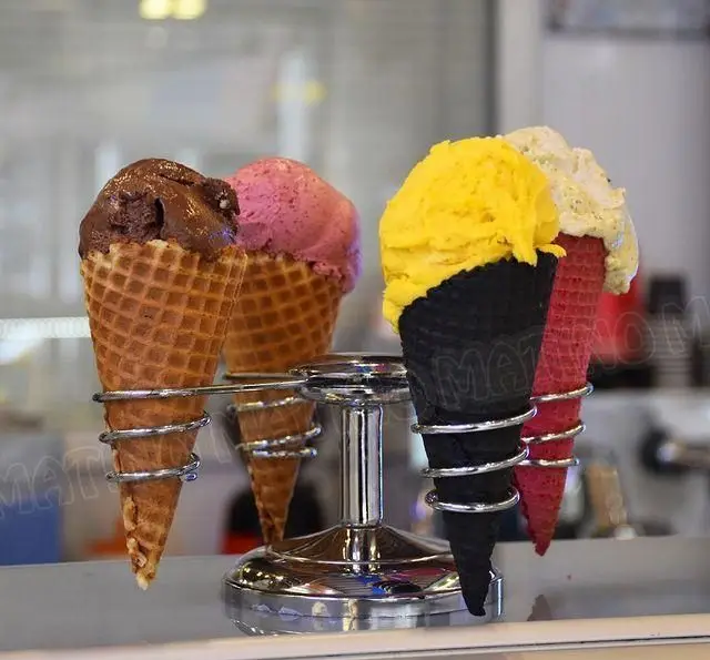 چندین بستنی قیفی خوشمزه و رنگارنگ کافه جلاتو متینو با طعم‌های متنوع شکلاتی، صورتی، زرد و سفید در کن‌های زیبا و خاص.