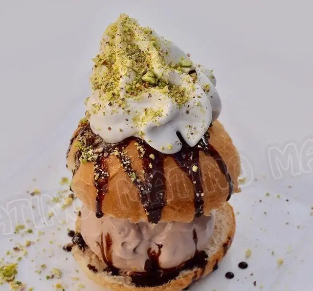 تصویری جذاب از ساندویچ جلاتو ویژه کافه متینو با بستنی شکلاتی، سس شکلات، خامه و پسته فراوان. تجربه دسرهای خاص جلاتو در کافه جلاتو متینو.