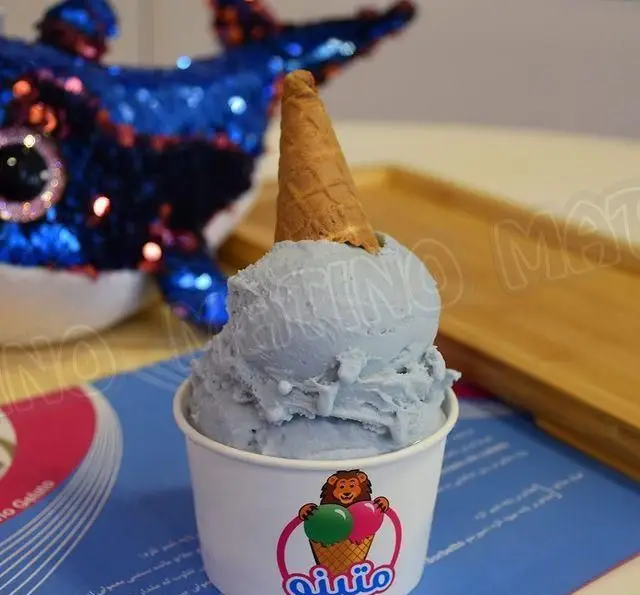 جلاتو خوش‌رنگ آبی روشن (Sky Blue) کافه جلاتو متینو با قیف بستنی روی آن، داخل فنجانی با لوگوی شیر و دو اسکوپ بستنی.