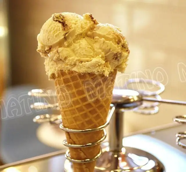 بستنی قیفی خوشمزه جلاتو متینو با اسکوپ‌های کرم رنگ وانیلی و تکه‌های مغزی، آماده سرو در پایه مخصوص کافه. دسر خنک تابستانی.