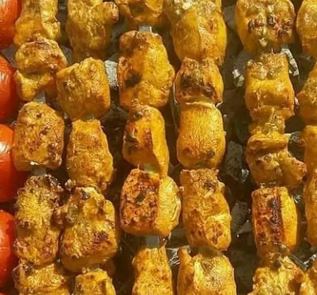 تصویری از سیخ‌های جوجه کباب و گوجه کبابی تازه و خوشمزه جگرکی گل یخ، در حال گریل شدن روی آتش ذغال. آماده برای یک وعده عالی.