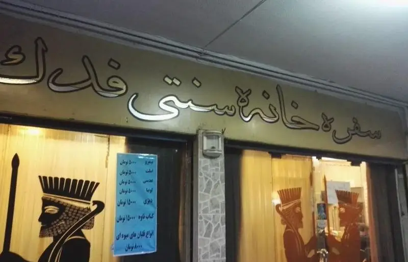 تابلو و ورودی سفره خانه سنتی فدک که غذاهای سنتی و انواع قلیان میوه‌ای ارائه می‌دهد، با دکوراسیون الهام‌گرفته از ایران باستان.