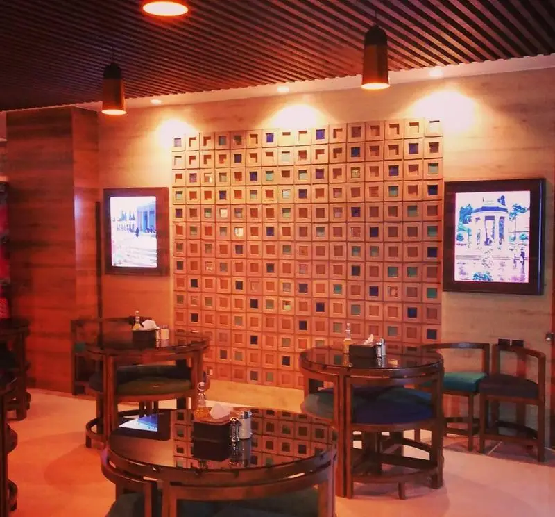 تصویری از محیط گرم و سنتی رستوران ترخون شیراز، شامل میز و صندلی‌های چوبی و دیوار دکوراتیو منحصر به فرد با نورپردازی آرامش‌بخش.