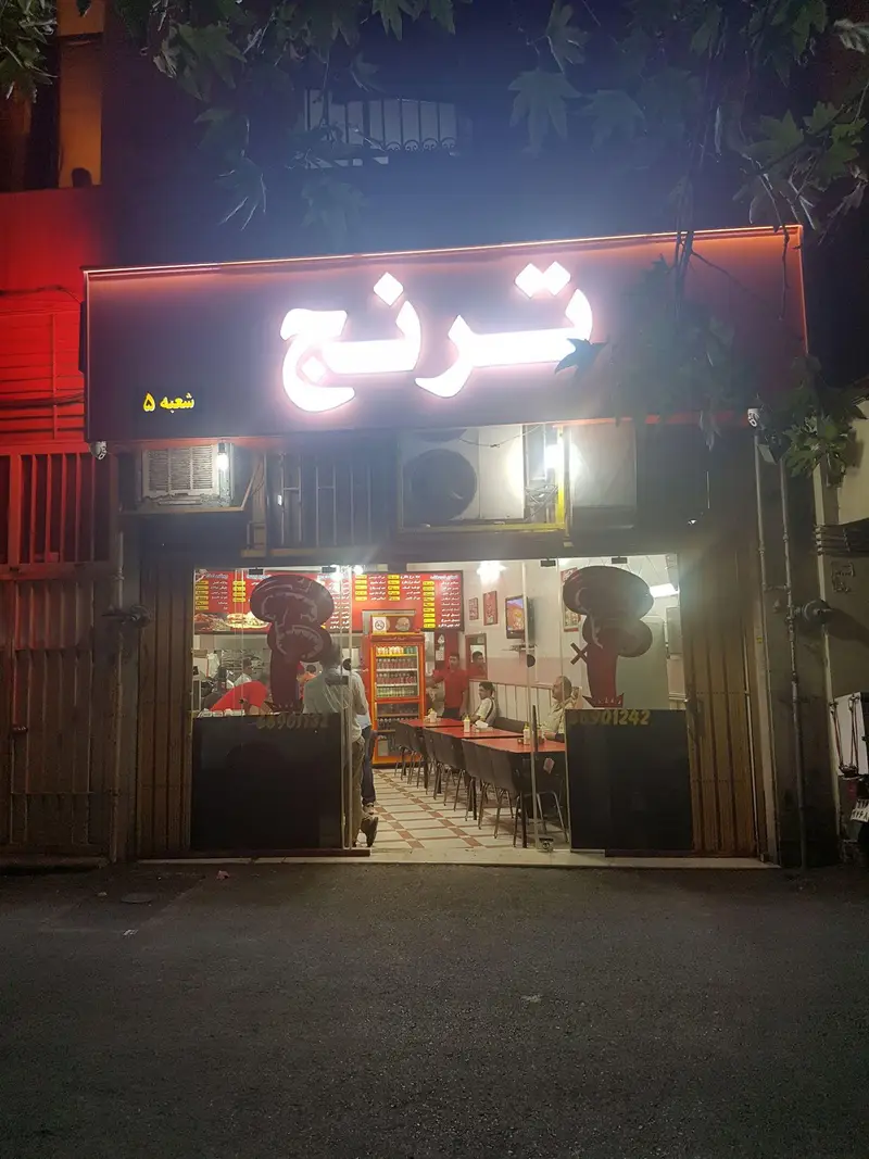 نمای شبانه و درخشان پیتزا ترنج شعبه ۵، یک رستوران فست فود پر جنب و جوش، با تابلوی روشن، فضای داخلی و مشتریان.