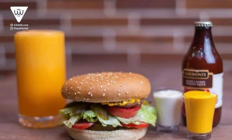 همبرگر خوشمزه سیب ۳۶۰ با نان کنجدی، کاهو، گوجه و پنیر، همراه آب پرتقال تازه و نوشیدنی‌های متنوع. تجربه فست فود لذیذ.