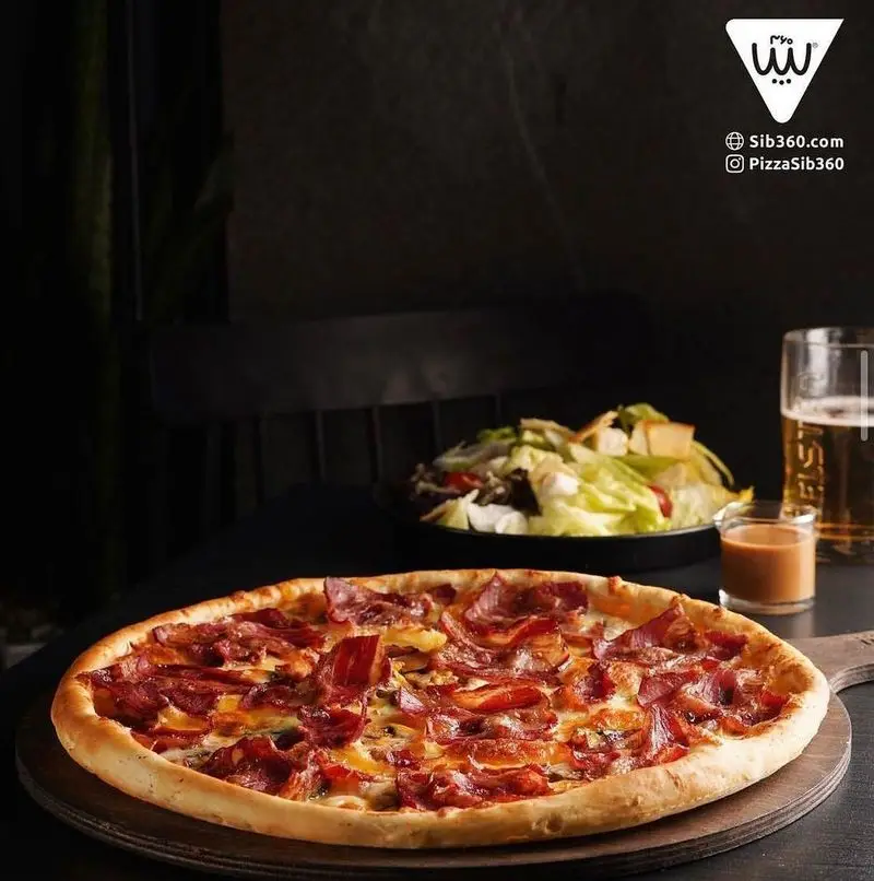 پیتزای بیکن خوش طعم سیب ۳۶۰ به همراه سالاد تازه و آبجو، آماده سرو در محیط دلپذیر رستوران سیب ۳۶۰.