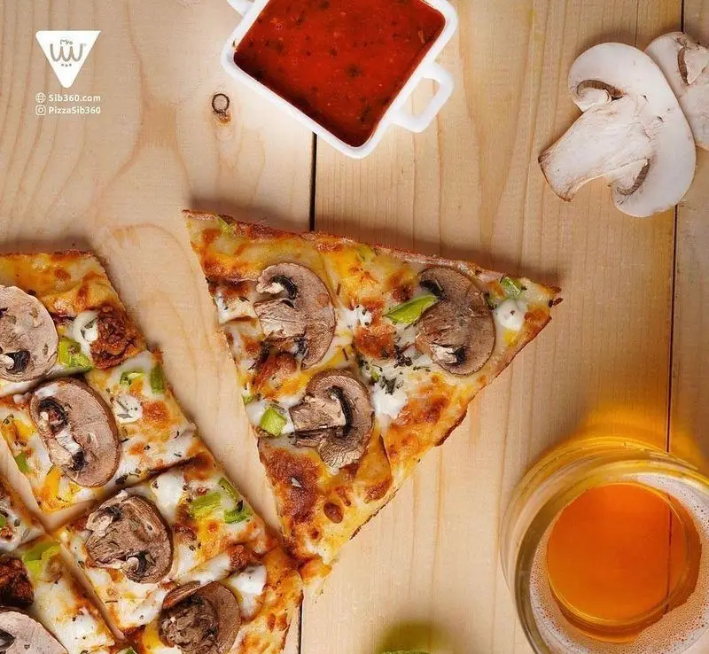 پیتزا قارچ و گوشت سیب ۳۶۰ برش خورده با پنیر آب شده، فلفل دلمه‌ای، روی میز چوبی، کنار سس، قارچ تازه و نوشیدنی.