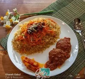 قابلی پلو خوش‌عطر و لذیذ افغانی با گوشت و تزئینات هویج، کشمش و آجیل در کنار خورشت در کافه رستوران خانه کابل.