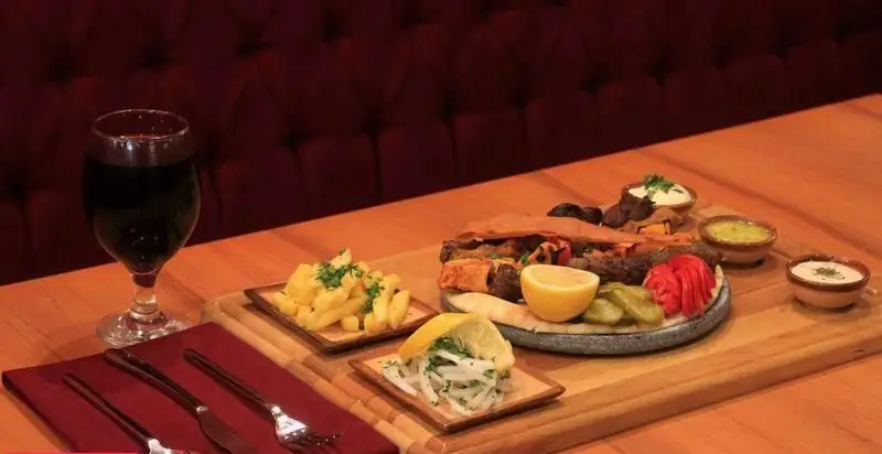 بشقاب کباب‌های لذیذ و سیب‌زمینی سرخ‌کرده در رستوران فرنگی آریل، همراه با نوشیدنی و سس‌های متنوع، تجربه‌ای فراموش‌نشدنی.