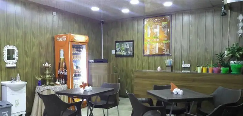 فضای داخلی دنج رستوران ماهان درباری با میز و صندلی، یخچال نوشیدنی، منوی غذا، پیشخوان و گلدان‌های رنگی. محیطی آرام برای صرف غذا.