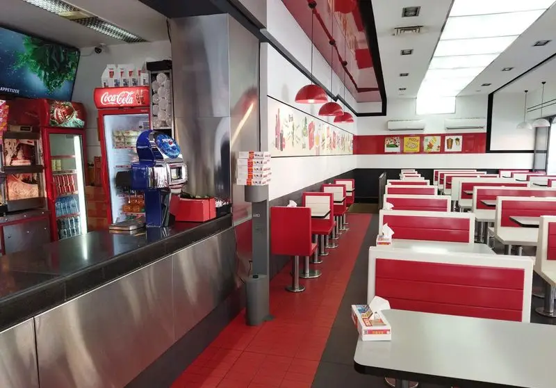 فضای داخلی مدرن و تمیز فست فود پیتزا زرین با میز و صندلی‌های قرمز و سفید، آماده برای سرو لذیذترین پیتزاها و غذاها.