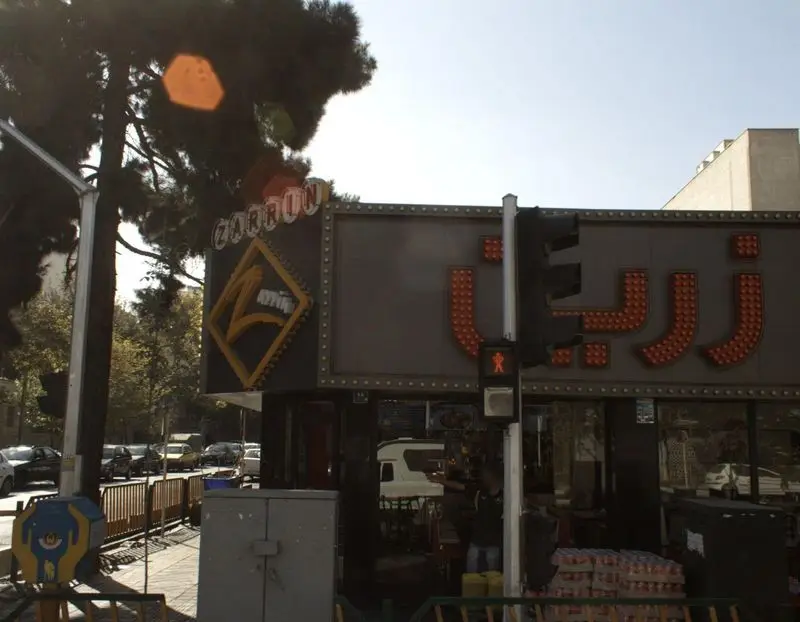 تصویری از نمای بیرونی فست فود پیتزا زرین در یک روز آفتابی، با تابلوی بزرگ و چشم‌نواز "زرین" به فارسی و انگلیسی در مرکز