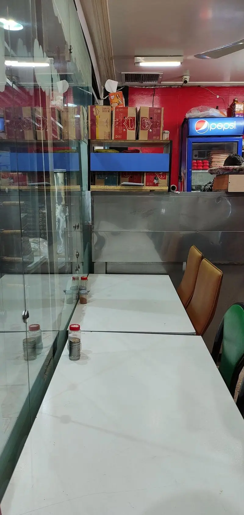 فضای داخلی پیتزا میلاد: میز و صندلی‌های تمیز آماده پذیرایی از مشتریان، همراه با پیشخوان سفارش و یخچال پپسی. دکوراسیون ساده و کاربردی.