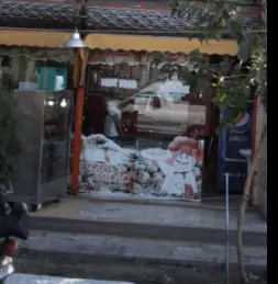 نمای بیرونی مغازه فست فود پیتزا میلاد با سایبان زرد، تابلو بزرگ تبلیغاتی، ویترین، یخچال نوشابه پپسی و ورودی پله‌دار برای مشتریان.