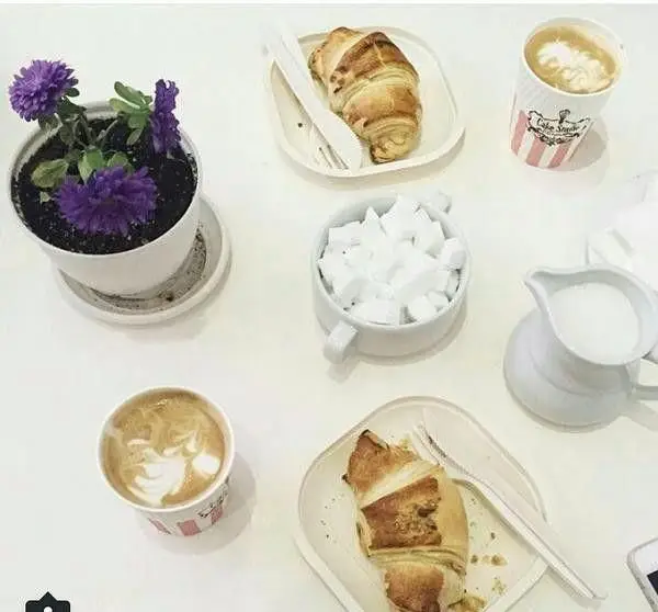 صبحانه دلچسب در کافه قنادی ورتا: قهوه تازه و کروسان طلایی با گلدان گل بنفش، محیطی آرام و دلنشین برای مشتریان.