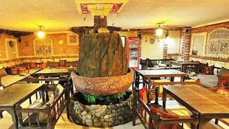 سفره خانه چار دیواری: فضای داخلی دلنشین با دکوراسیون سنتی و آجرکاری، آبنمای سنگی مرکزی، میزها و تخت‌های چوبی راحت برای میزبانی.