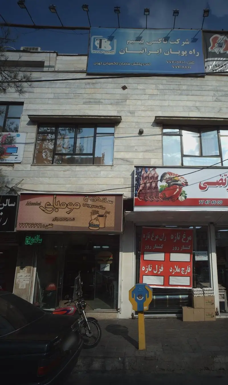 نمای بیرونی ساندویچ فروشی مومبای در تهران، فست فود محبوب با تابلوی شامل همبرگر، سیب زمینی و نوشیدنی. ساندویچی خوب.
