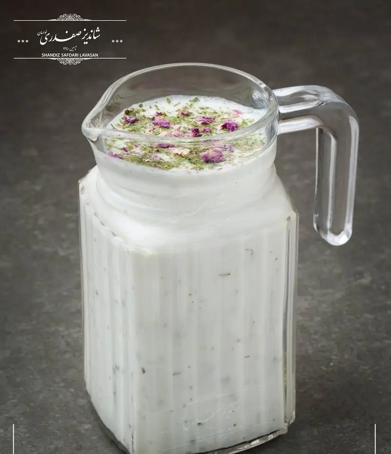 دوغ خوش طعم و خنک شاندیز صفدری لواسان در پارچ شیشه‌ای، با تزیین گل محمدی و نعنا خشک، نوشیدنی اصیل ایرانی.