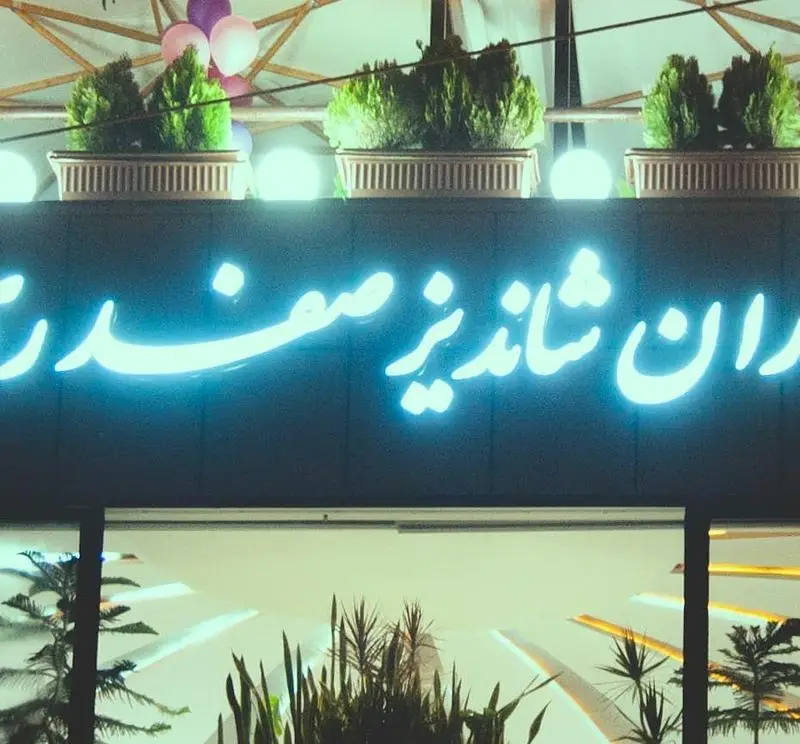 تابلوی نئونی درخشان رستوران شاندیز صفدری با طراحی مدرن و نور آبی چشم‌نواز، به همراه فضای سبز و دکوراسیون بیرونی زیبا در شب