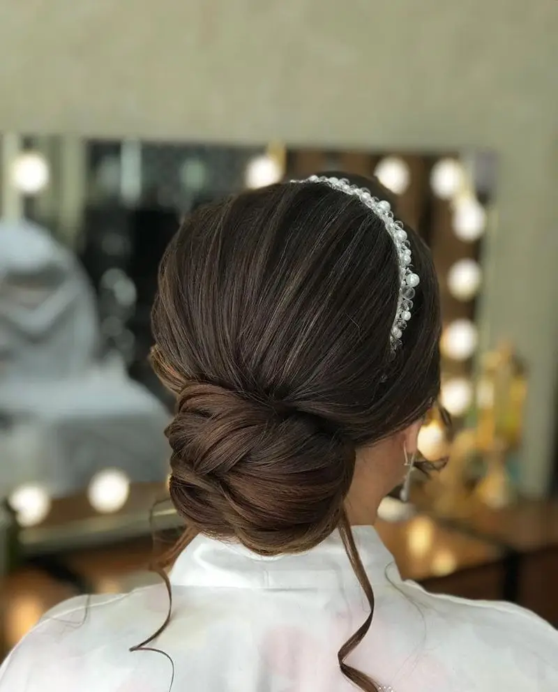 شینیون شیک و مجلسی، بافته شده با ظرافت، مناسب برای عروس و مهمانی در آرایشگاه زنانه آنا. همراه با هدبند مروارید.