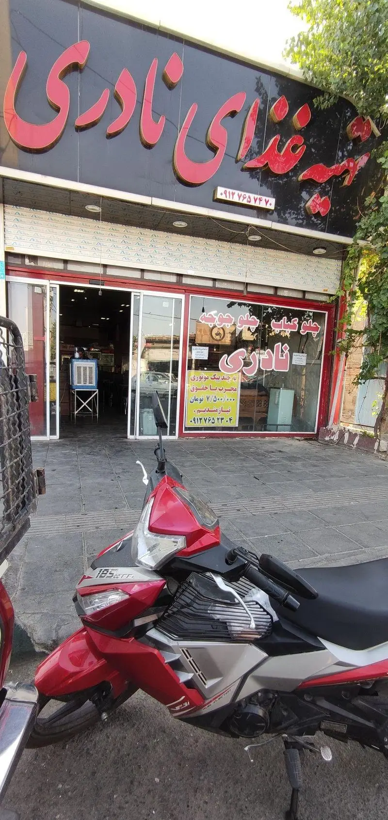 نمای بیرونی تهیه غذای نادری، متخصص چلو کباب و چلو جوجه، با تابلوی فارسی قرمز رنگ و ورودی شیشه‌ای. یک موتورسیکلت جلوی مغازه پارک شده.