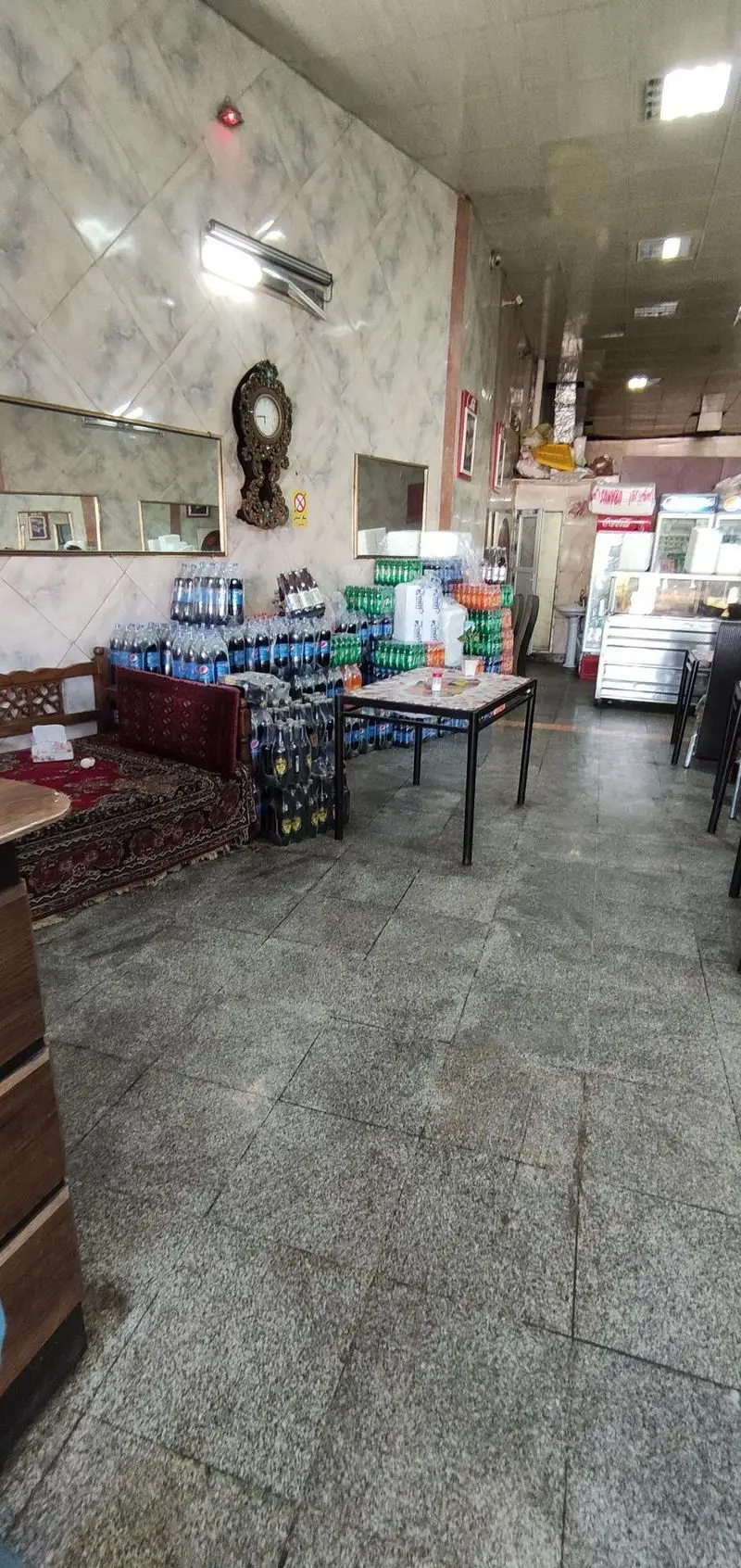 تصویری از داخل تهیه غذای نادری با قفسه‌های نوشیدنی‌های متنوع، فضای نشیمن سنتی و میزهای غذاخوری. آماده ارائه سرویس غذا.