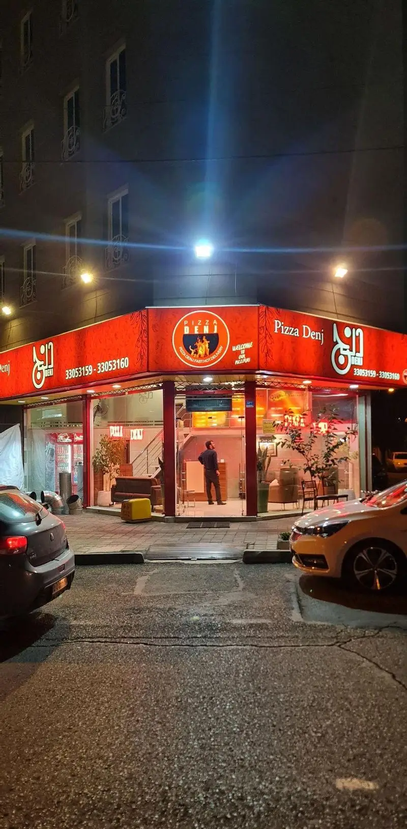 نمای بیرونی پیتزا دنج، رستوران فست فود در شب با تابلوهای روشن و شماره تماس‌های 33053159 و 33053160 جهت سفارش و دلیوری.