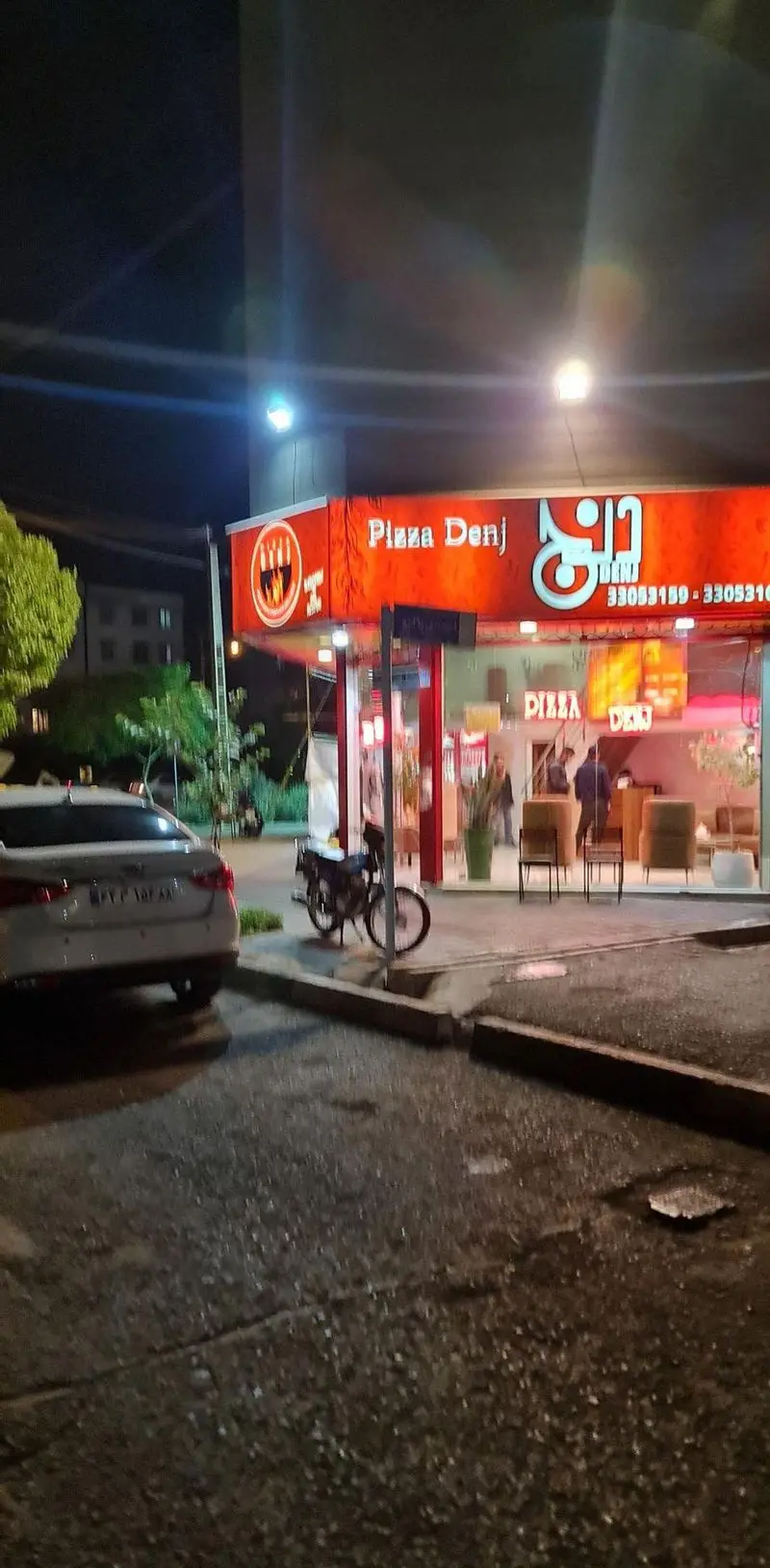 نمای شبانه از رستوران پیتزا دنج، یک فست فود محبوب با نورپردازی روشن و مشتریان در حال رفت و آمد.