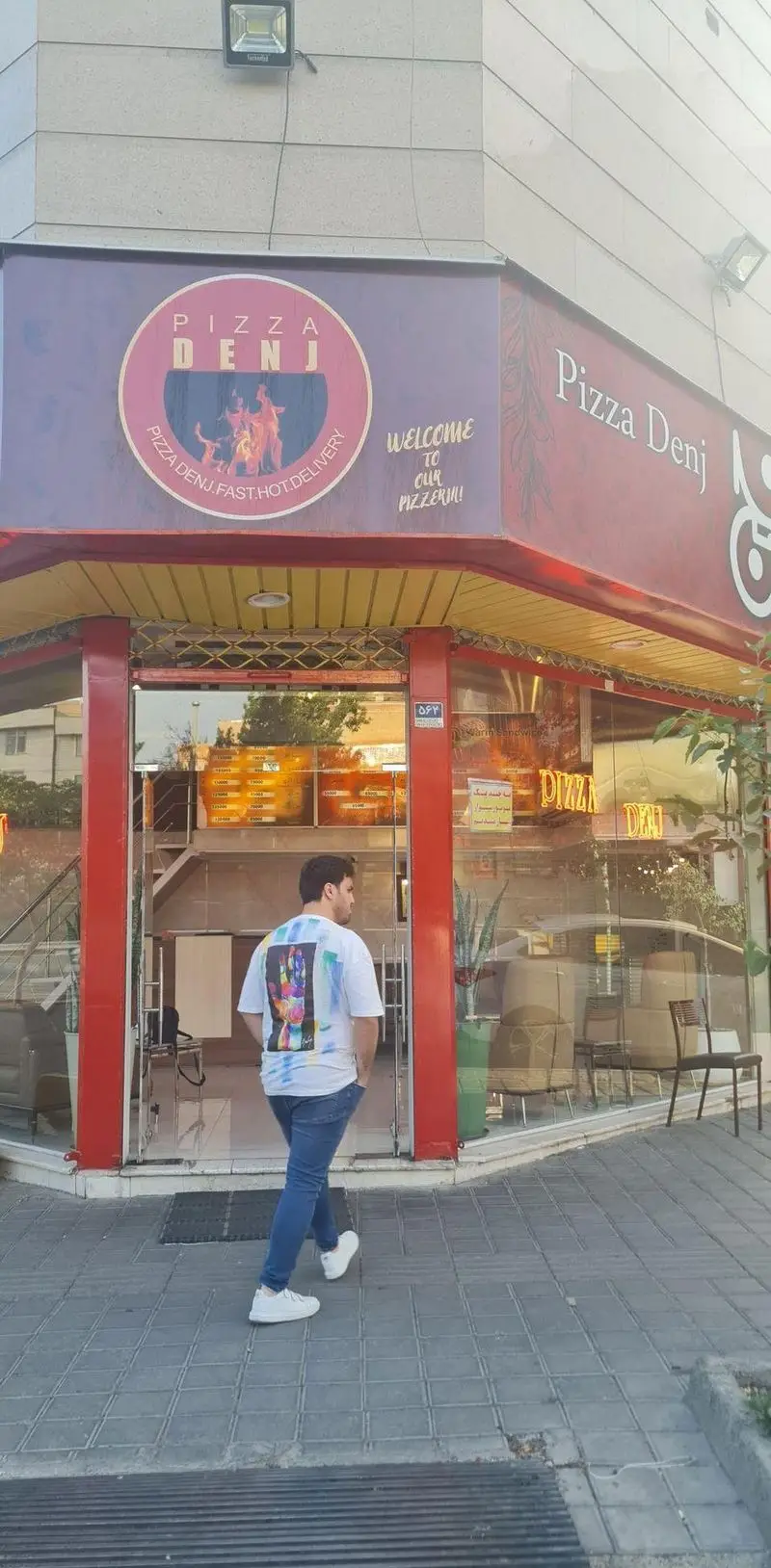 رستوران پیتزا دنج با تابلوی پیتزا دنج و شعار تحویل سریع. یک مرد از جلوی ورودی شیشه‌ای پیتزافروشی عبور می‌کند.