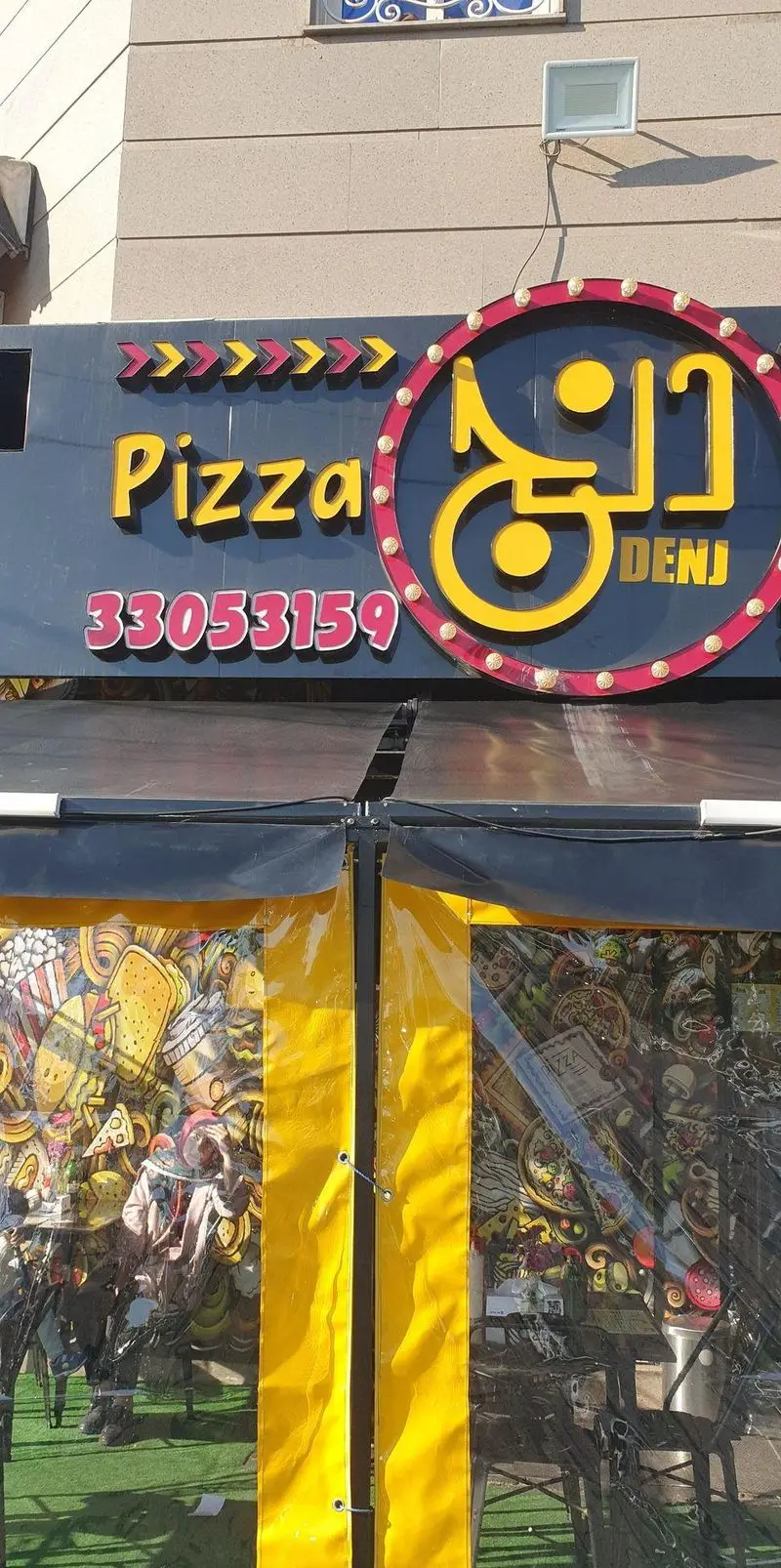 نمای نزدیک از تابلوی جذاب و رنگارنگ "پیتزا دنج" با نام "Pizza Denj" و شماره تماس 33053159. یک کسب و کار فست فود تخصصی پیتزا.