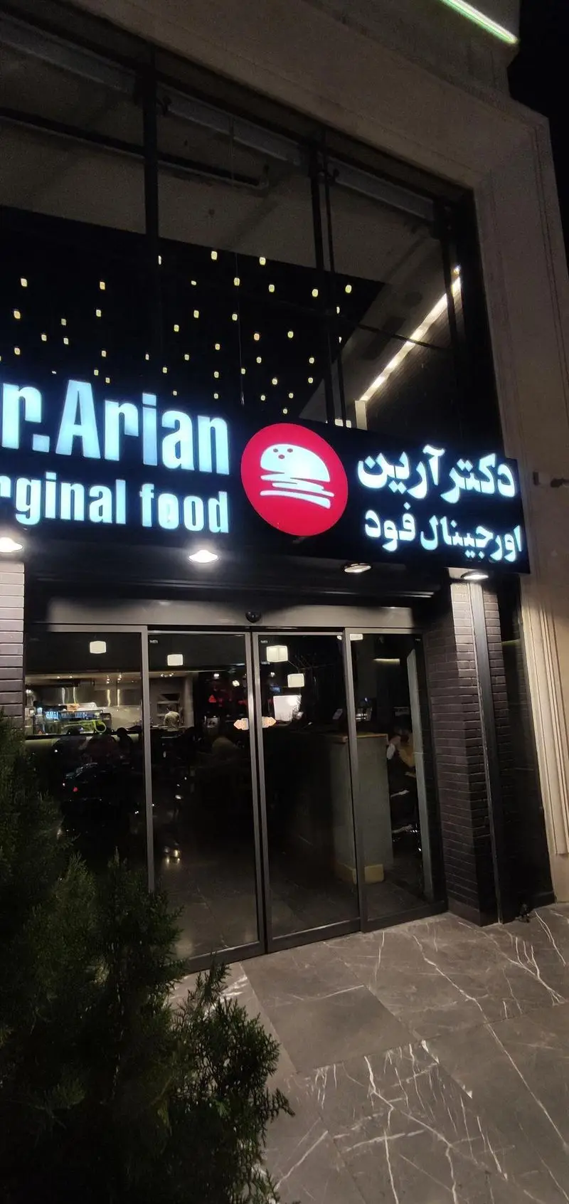 نمای بیرونی و تابلوی درخشان فست فود دکتر آرین در شب، با شعار "Original food" و لوگوی برجسته برگر، آماده استقبال از مشتریان.