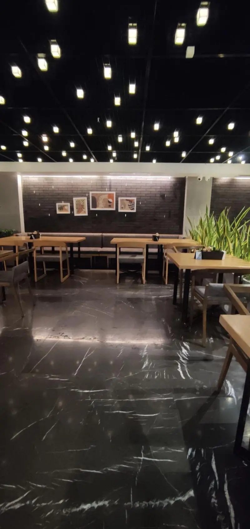 تصویری از فضای داخلی مدرن و دلپذیر فست فود دکتر آرین با چیدمان میز و صندلی‌های چوبی، کفپوش مرمریت و نورپردازی سقف.