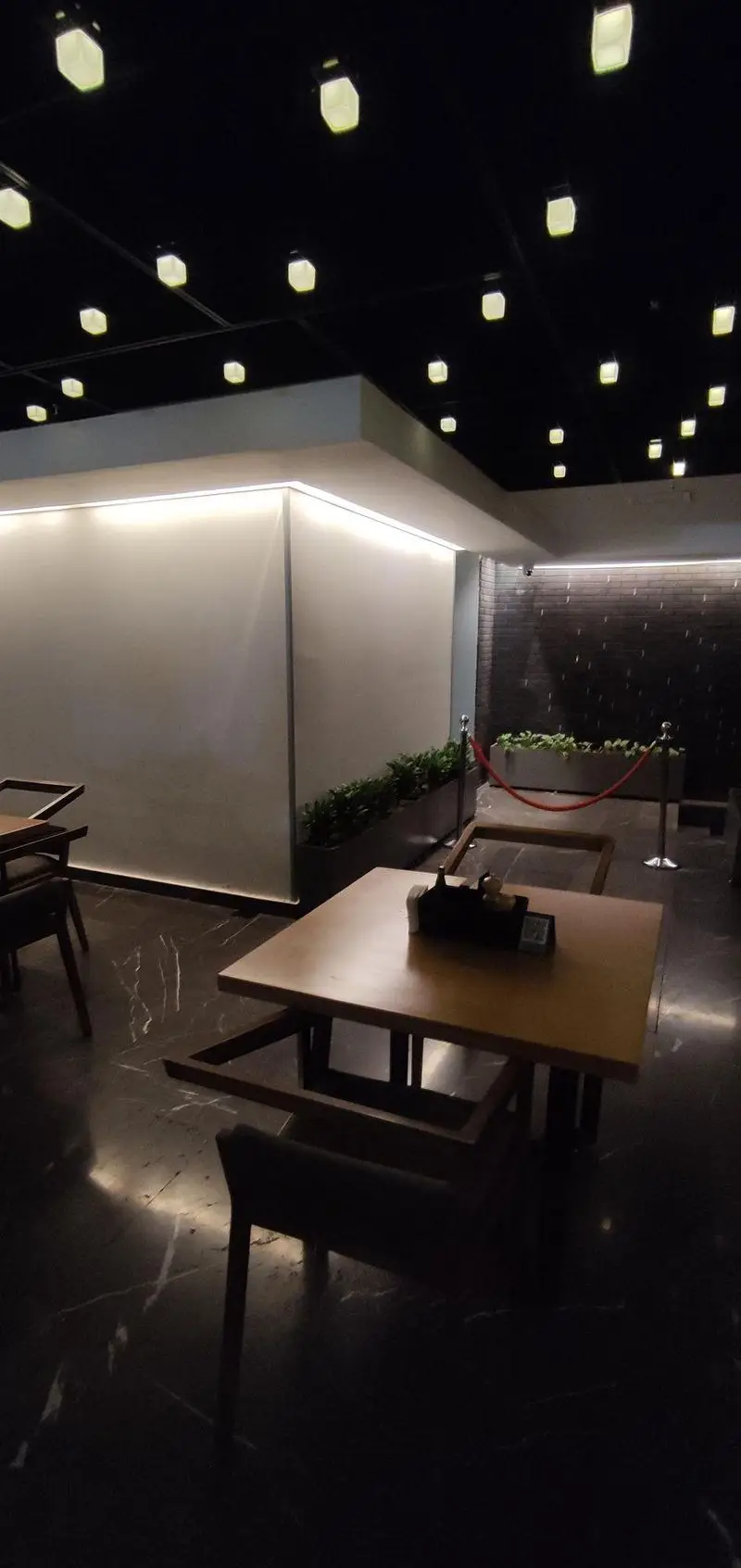 محیط داخلی مدرن و دنج فست فود دکتر آرین با نورپردازی سقفی و نوارهای نوری دیواری، میزهای چوبی و کفپوش سنگی.