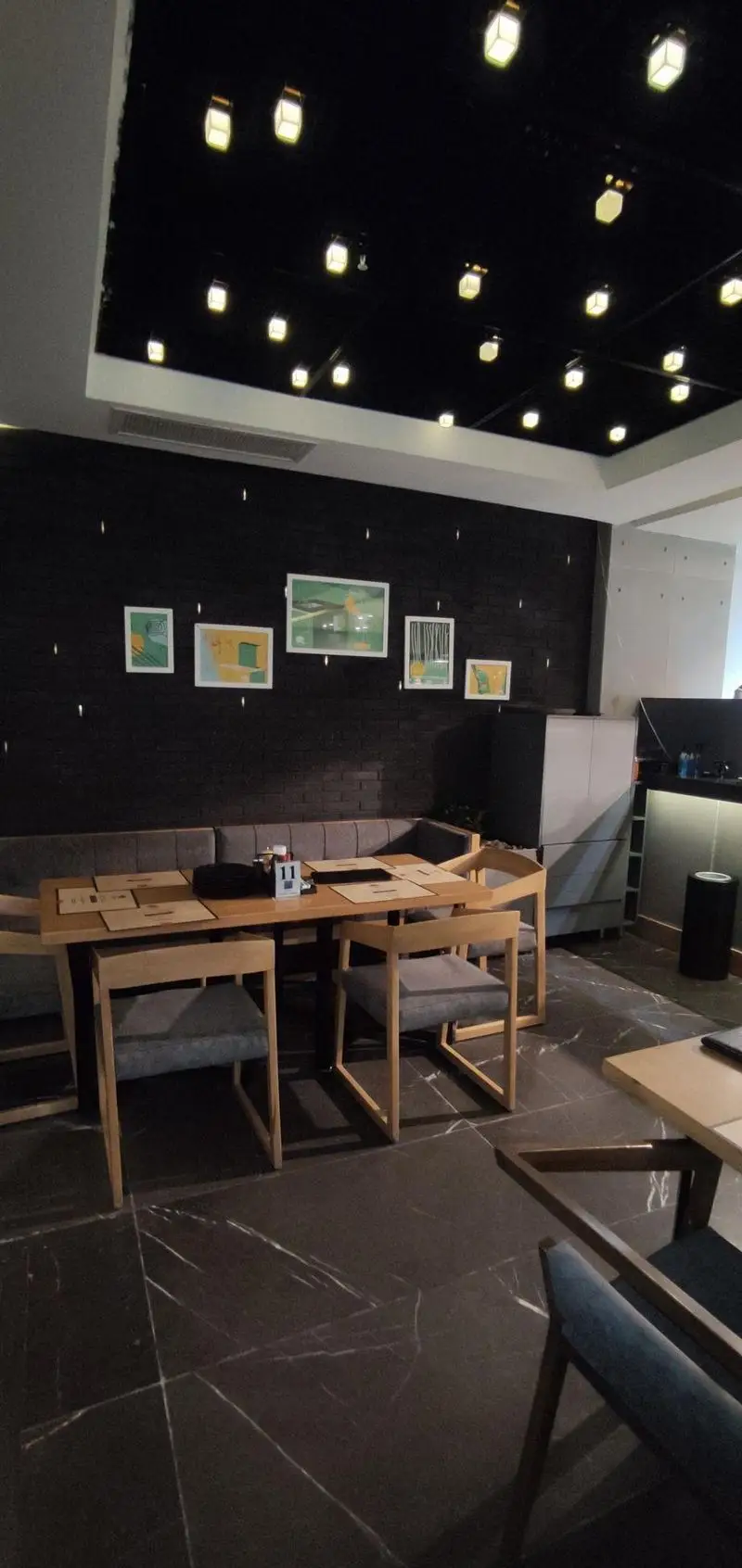 فضای داخلی دلنشین و مدرن فست فود دکتر آرین، شامل میز و صندلی چوبی، نورپردازی سقفی خاص و دیوارهای تیره با تابلوهای هنری.