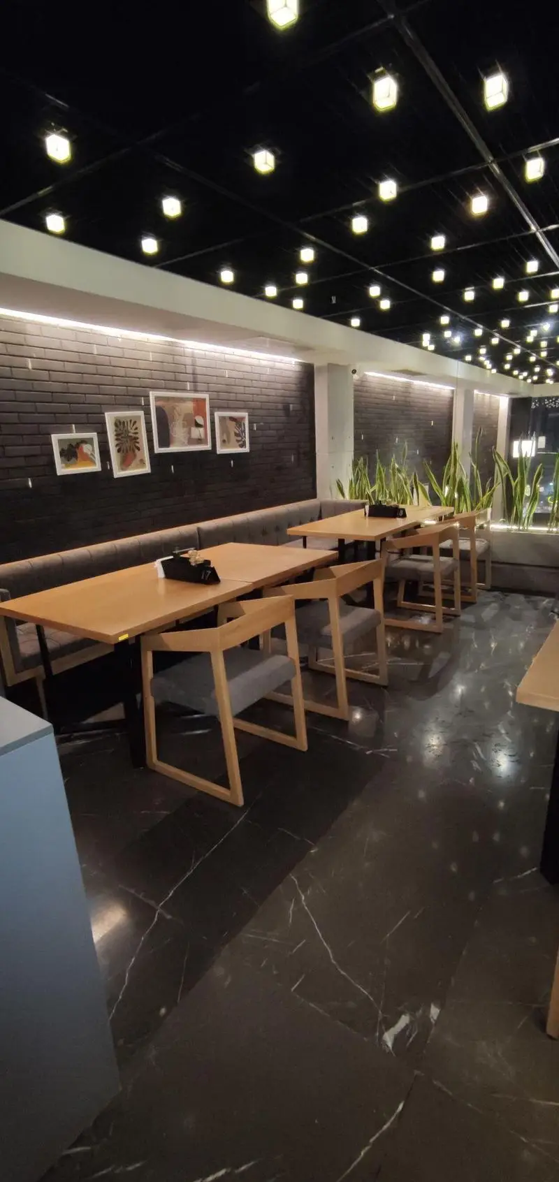 تصویری از فضای داخلی مدرن و جذاب فست فود دکتر آرین با دکوراسیون دیوارهای آجری مشکی، میز و صندلی‌های چوبی و نورپردازی زیبا.