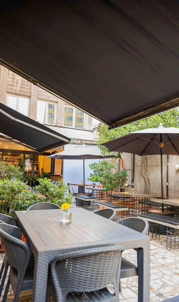 فضای بیرونی کافه رام بیسترو با چیدمان زیبا و دلنشین، میز و صندلی‌های راحت، چترهای بزرگ، و گل و گیاه برای سرو انواع غذا و نوشیدنی.