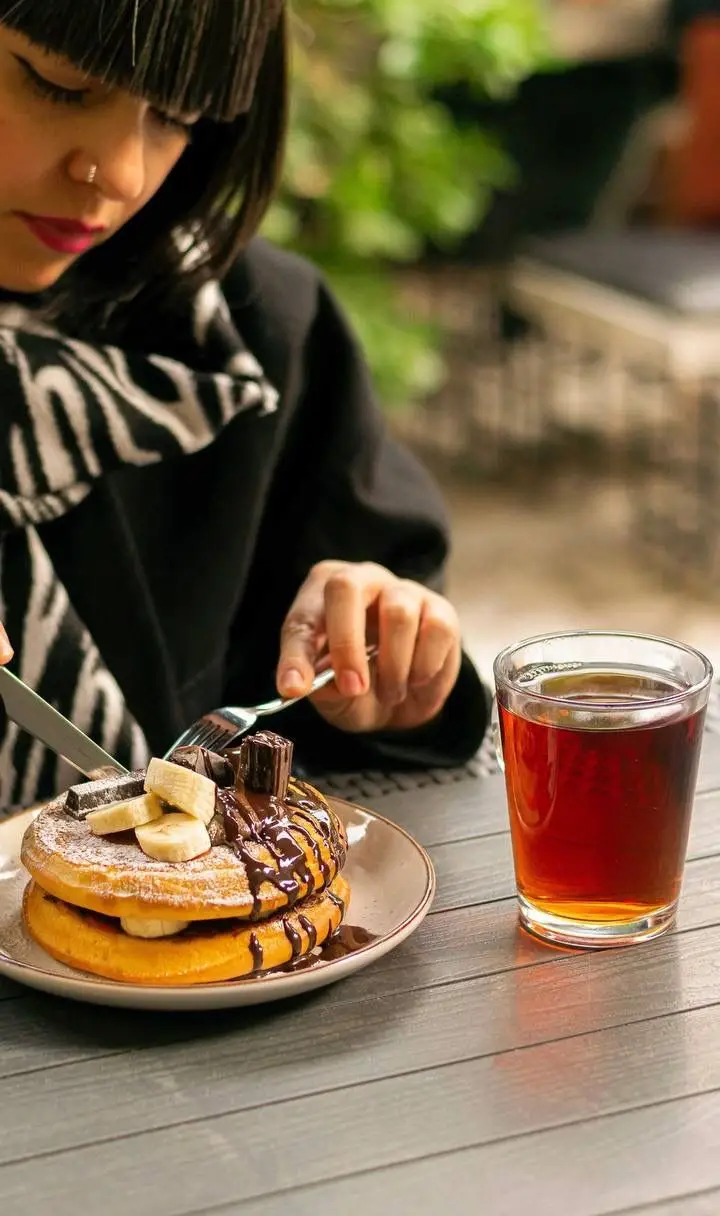 مشتری در کافه رام بیسترو در حال لذت بردن از پنکیک شکلاتی با موز و چای، ترکیبی دلپذیر از غذا و نوشیدنی برای یک تجربه آرامش‌بخش.