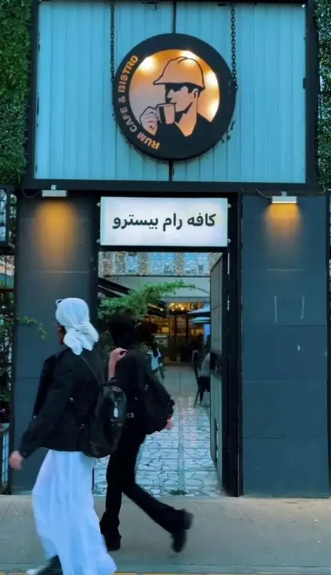 کافه رام بیسترو با تابلوهای روشن و لوگوی مرد با فنجان، مکانی دلنشین برای صرف انواع غذاها و نوشیدنی‌های متنوع.