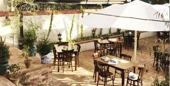 پیتزایی طلوع: فضای روباز شیک و دنج با میز و صندلی‌های چوبی، چترهای بزرگ سفید، مناسب برای لذت بردن از پیتزا و نوشیدنی.