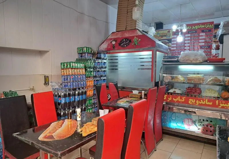 تصویری از فضای داخلی ساندویچی جمشید، شامل میز و صندلی‌های قرمز و مشکی، یخچال نمایش غذاهای تازه و نوشیدنی‌های متنوع چیده شده.
