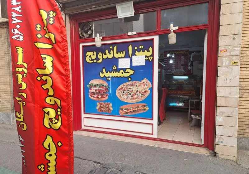 نمای بیرونی مغازه فست فود جمشید، شامل تابلوی پیتزا و ساندویچ با عکس برگر و ساندویچ و پیتزا، همراه بنر تبلیغاتی پیک رایگان و شماره تماس.