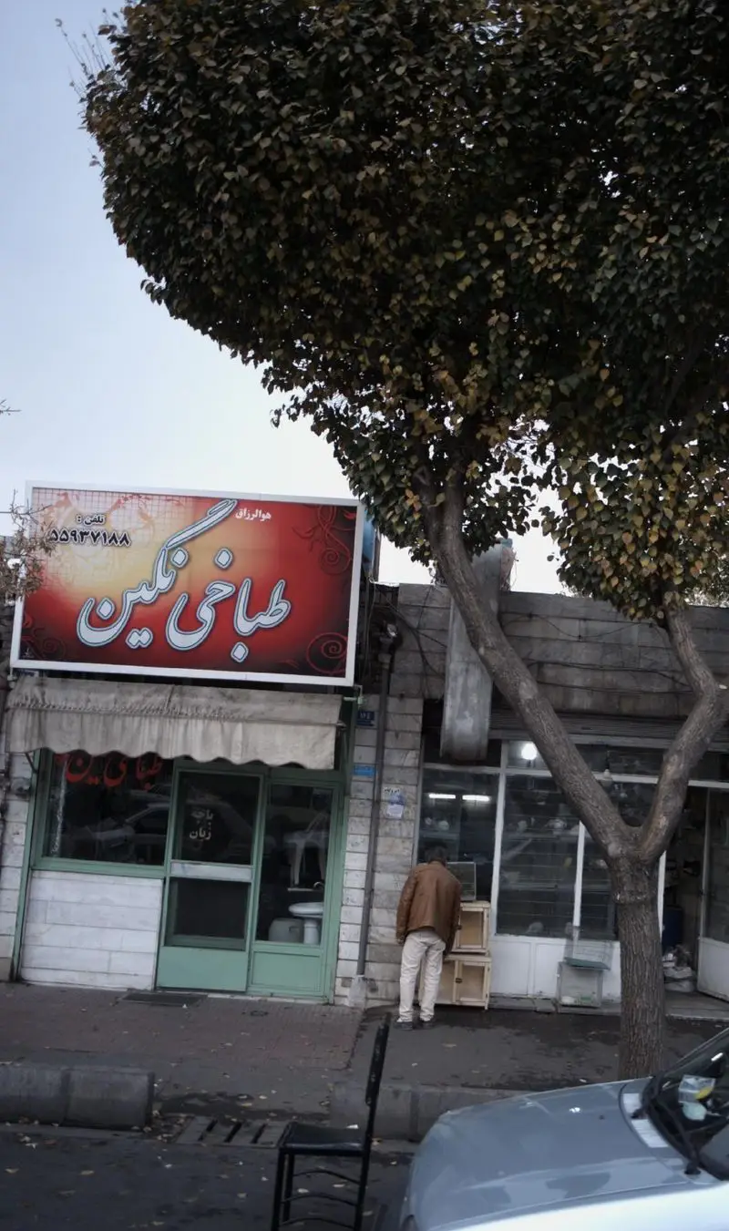 عکس از تابلوی شاخص طباخی نگین، با رنگ قرمز و فونت سفید برجسته، به همراه شماره تماس ۵۵۹۳۷۱۸۸ و نمای خیابان.