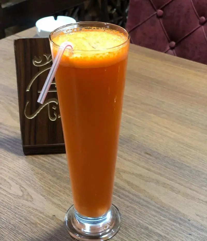 آب هویج تازه و طبیعی با نی، انتخابی سالم از منوی نوشیدنی‌های سفره خانه سنتی دیزی نار بر روی میز چوبی.