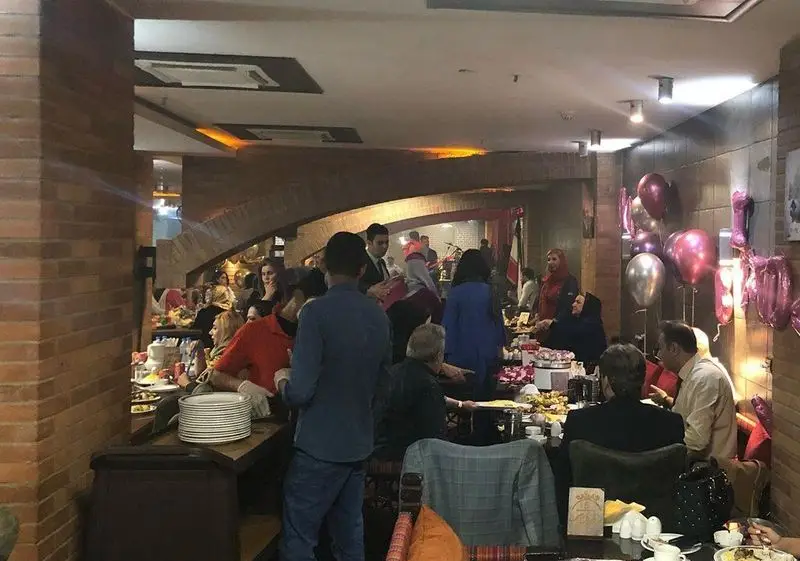 سفره خانه سنتی دیزی نار: دورهمی شاد میهمانان در فضایی گرم و سنتی با میزهای پر از غذا، دکوراسیون آجری و بادکنک‌های رنگارنگ.