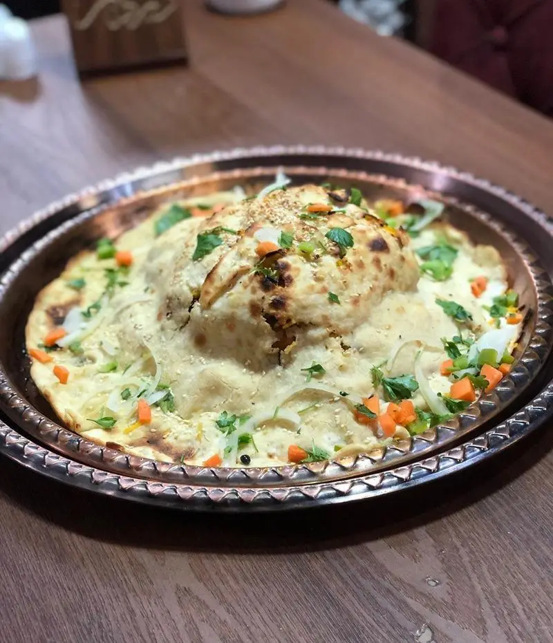 دیزی نار، غذای سنتی ایرانی با نان تازه، سبزیجات و ادویه‌های معطر در سینی مسی. تجربه طعم اصیل در سفره خانه سنتی دیزی نار.