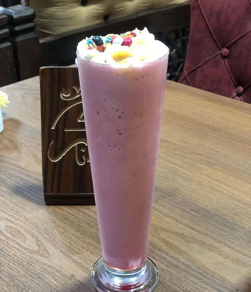 میلکشیک صورتی تازه و خوش‌طعم با خامه، اسپرینکلز رنگارنگ و میوه در سفره خانه سنتی دیزی نار. نوشیدنی خنک و دلپذیر.