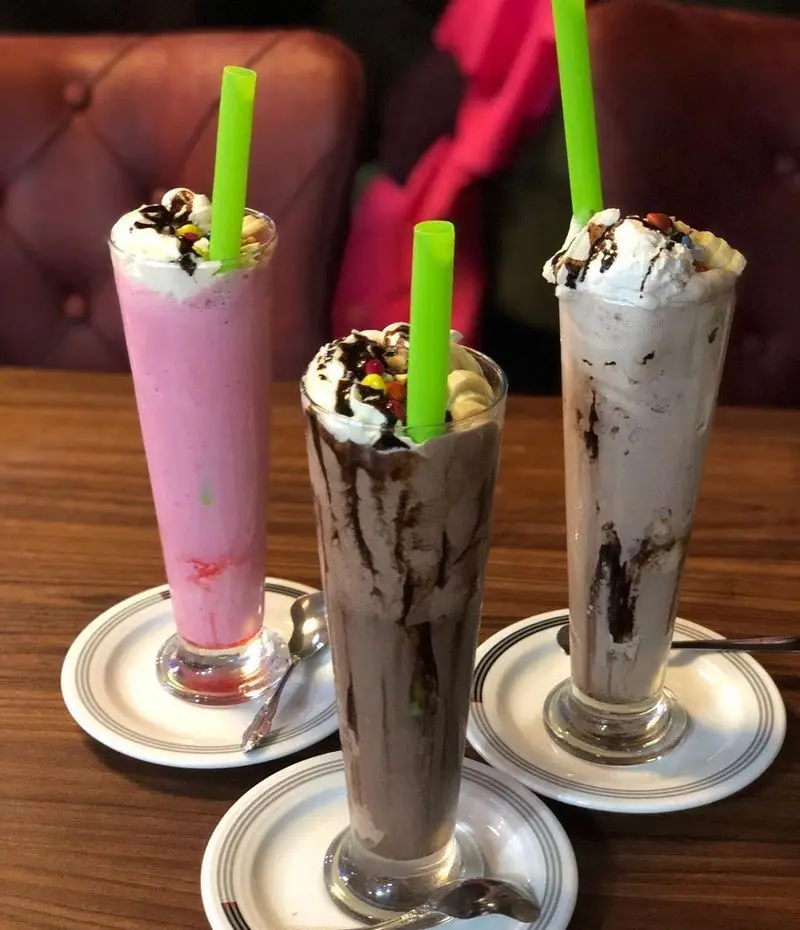 سه میلک شیک تازه و دلپذیر با طعم‌های توت فرنگی، شکلات و قهوه، با خامه فراوان و تزئینات زیبا در سفره خانه دیزی نار. لذت نوشیدنی‌های خنک.